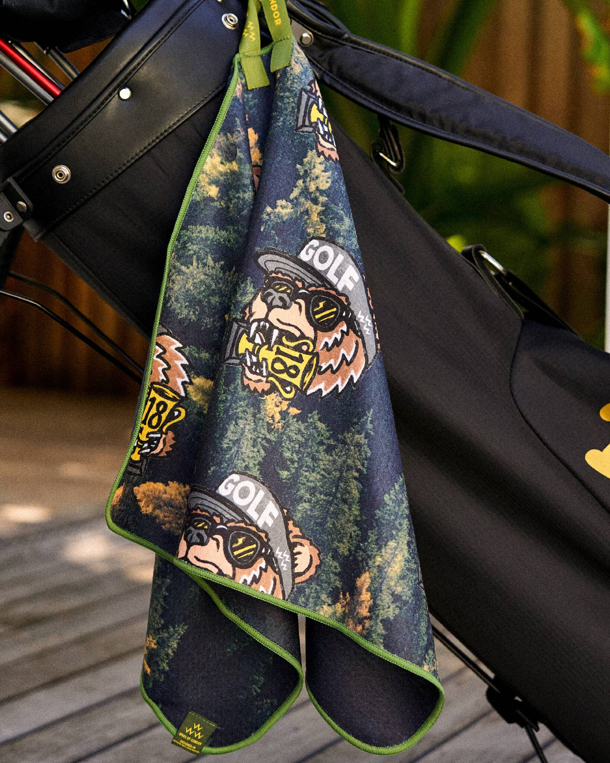 Black golf towel with a green border and a print of bears wearing hats, sunglasses, and biting trophies.
