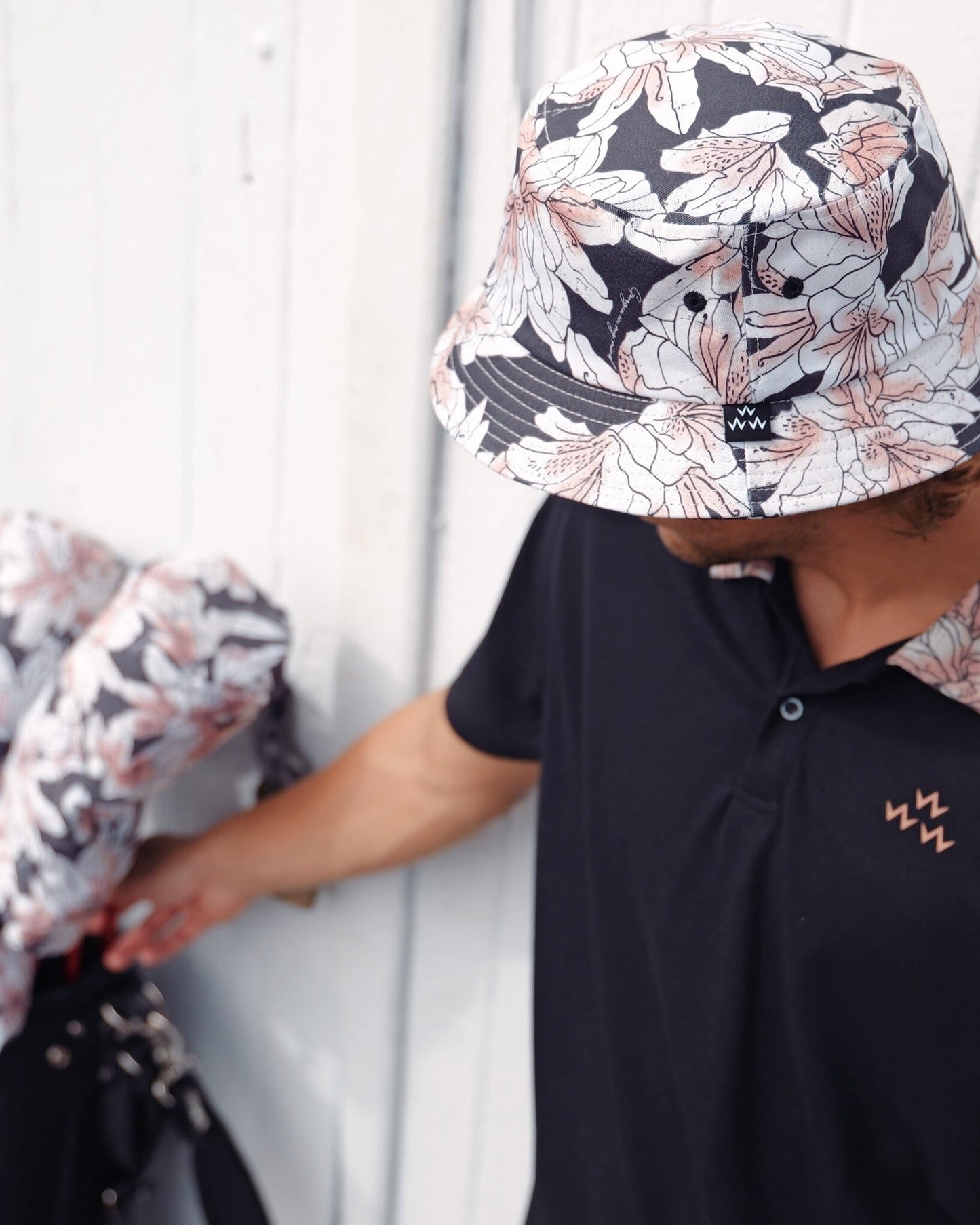 A person wearing a black bucket hat with a white and pink azalea print, next to a matching golf bag.