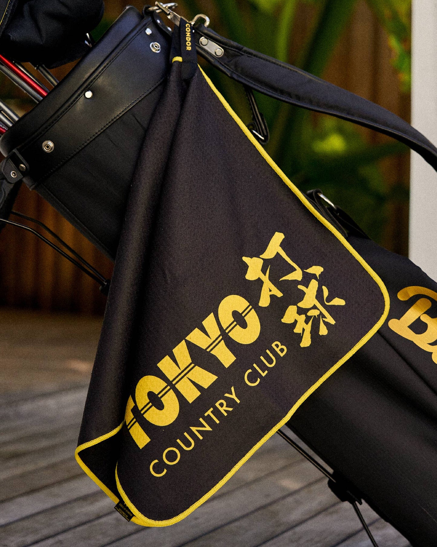 A black golf towel hanging from a golf bag, featuring yellow piping and a Tokyo Country Club graphic.