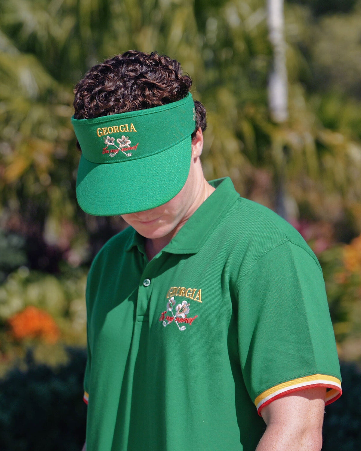 A person wearing a Masters Green visor featuring an embroidered Georgia On My Mind logo and matching polo.