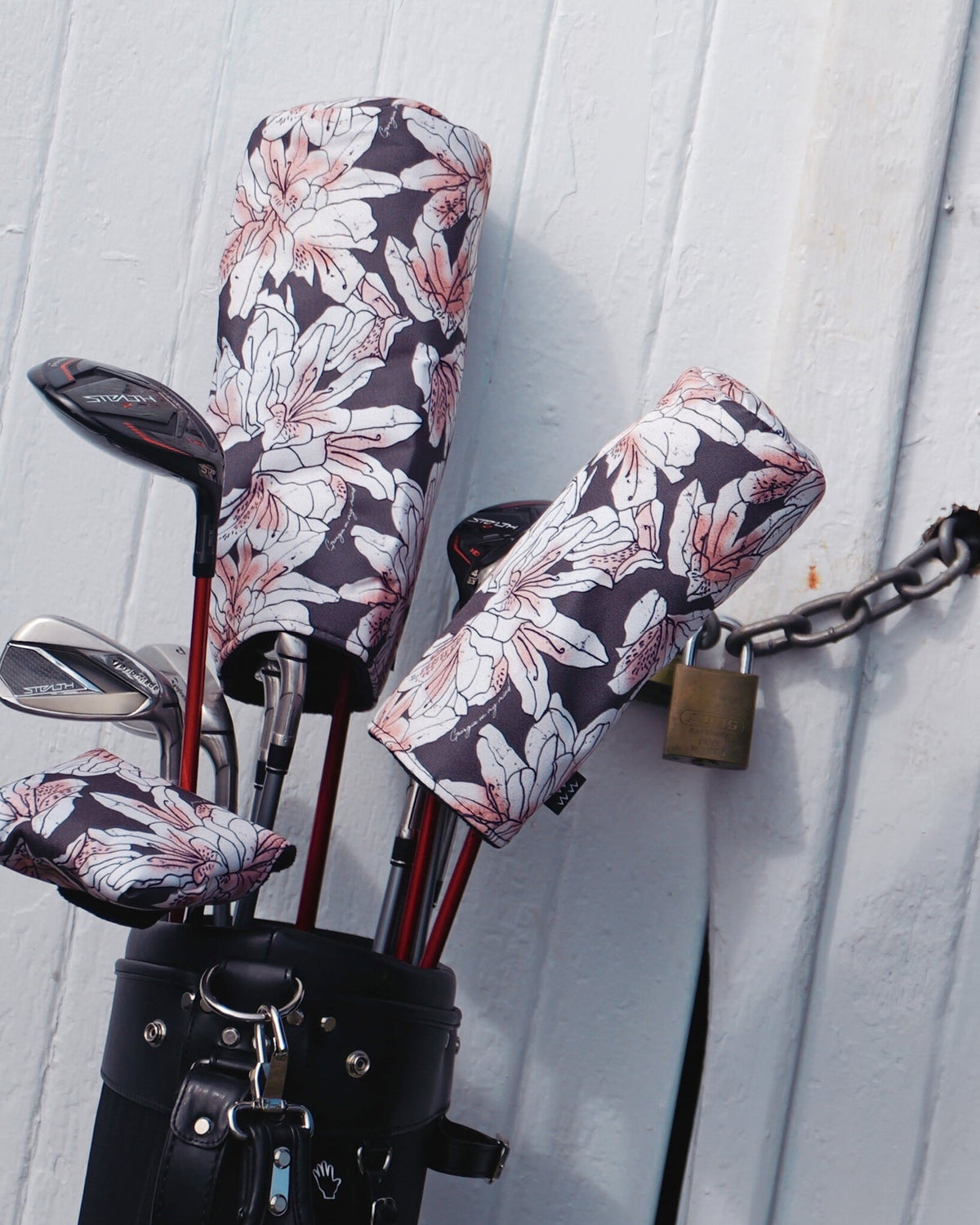 Golf clubs in a black bag feature azalea print headcovers with pink and white flowers against dark fabric.