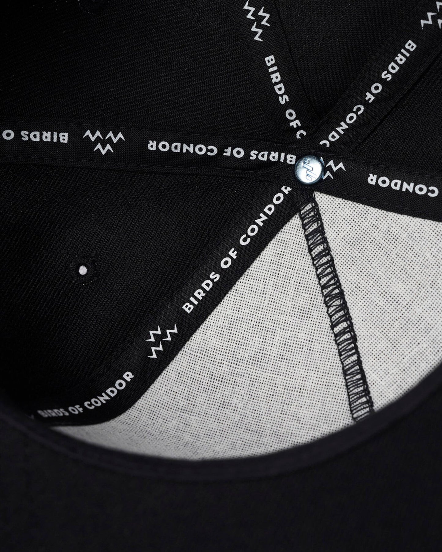 Detail of a black cap with interior branded taping featuring text reading BIRDS OF CONDOR and zigzag motifs.