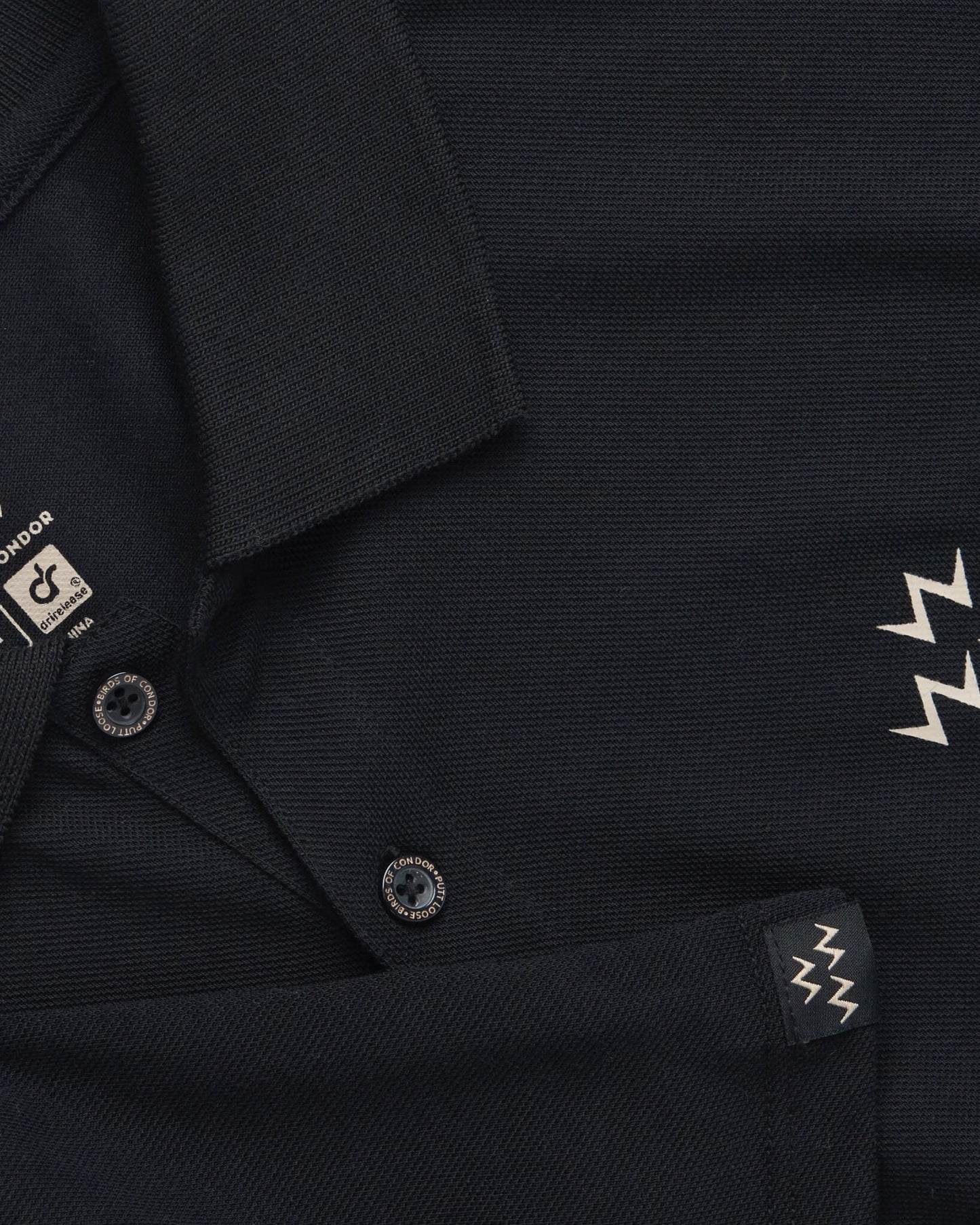 Detail of a black polo shirt featuring tan triple eagle print, collar, and branded tonal buttons.