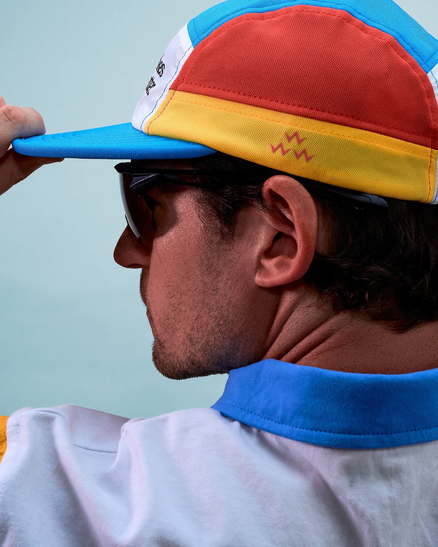 A person wearing a multi-colour sports cap in white, red, yellow, and blue with a flat brim.