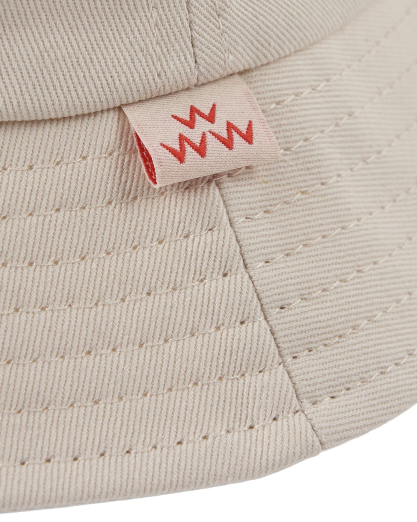 Detail of off-white cotton twill bucket hat with a small red woven label on the brim.