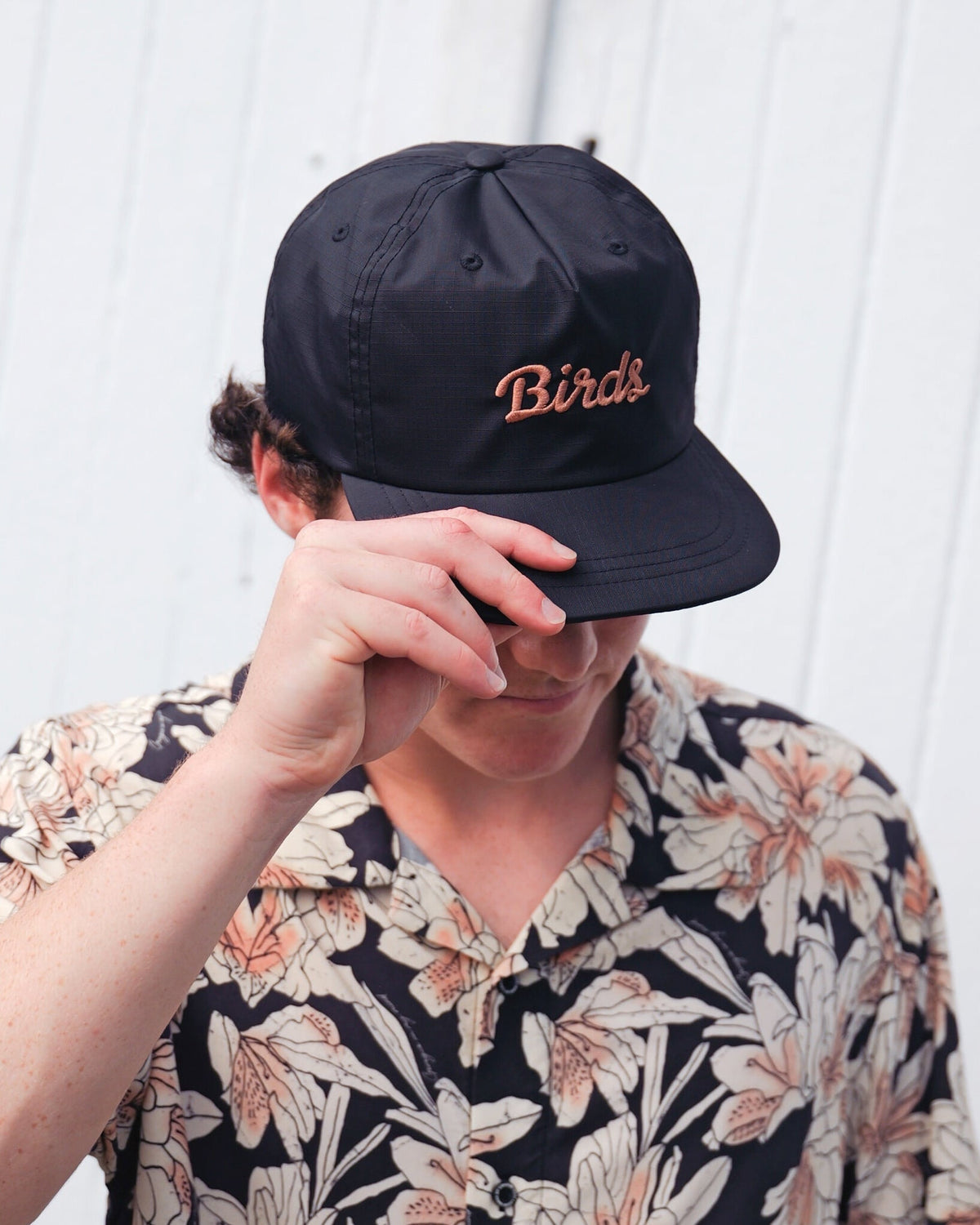 A person wearing a black snapback hat with the embroidered script text Birds on the front.