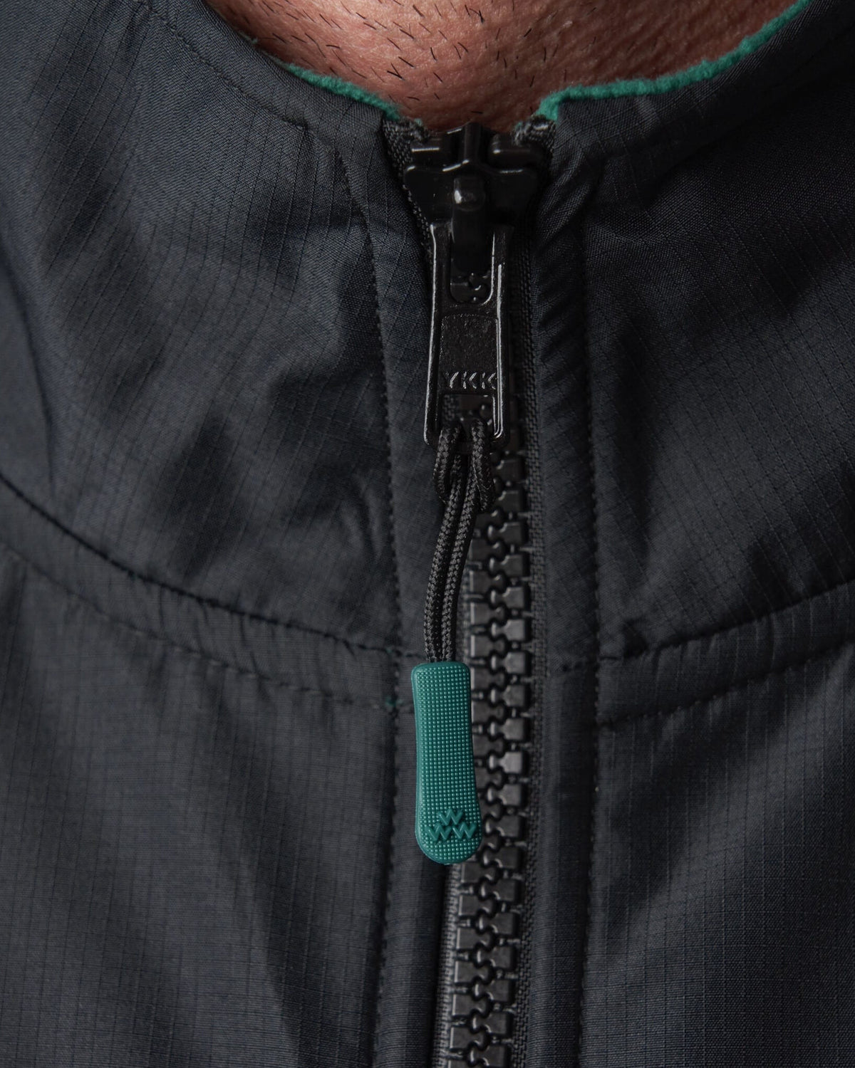 Detail of a dark green fleece sweater collar featuring a black zipper with a green pull tab.