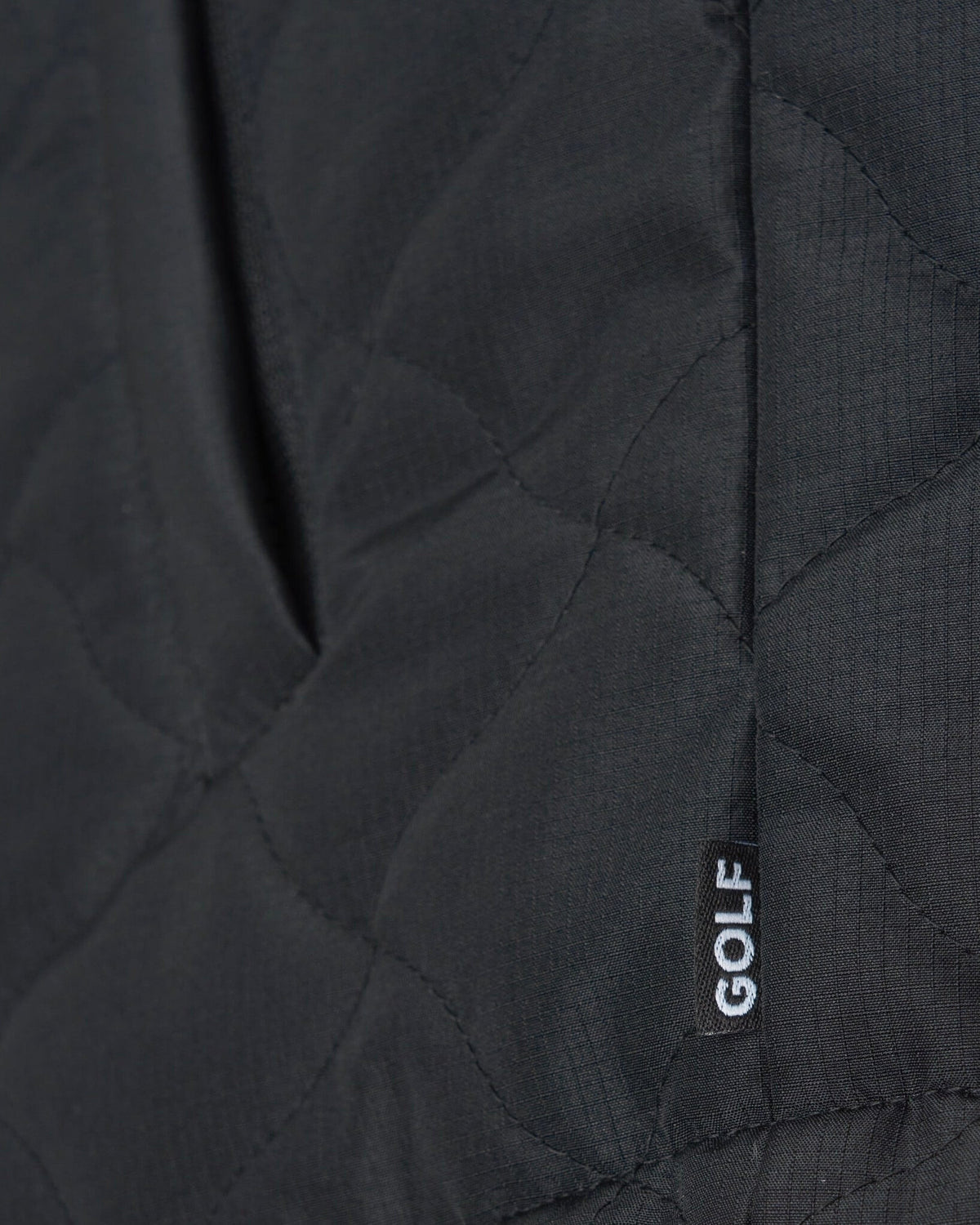 Detail of a black quilted vest featuring warped argyle stitching, a pocket, and a small black patch reading GOLF.