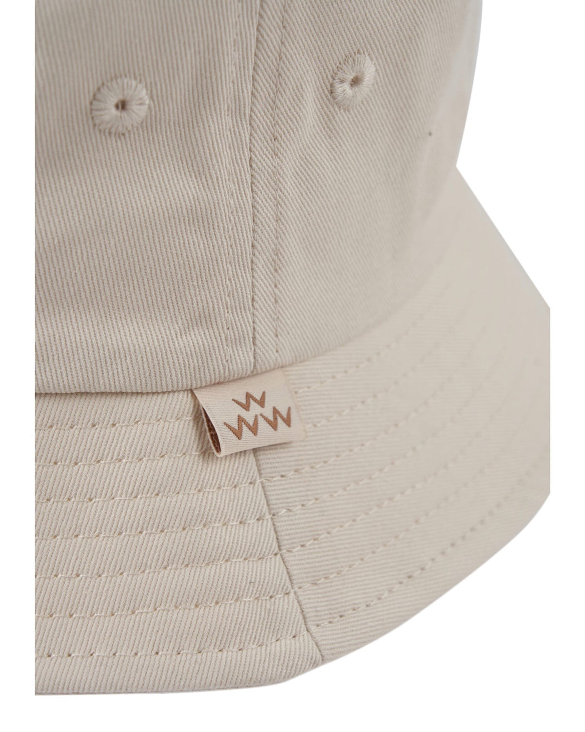 Detail of an off-white cotton bucket hat with a small logo tag stitched along the brim seam.