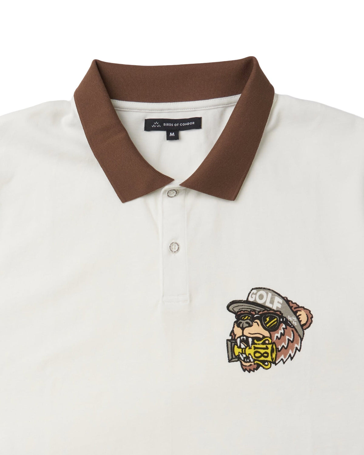 Detail of an off-white polo shirt featuring a brown ribbed collar, a two-button placket, and a bear graphic.