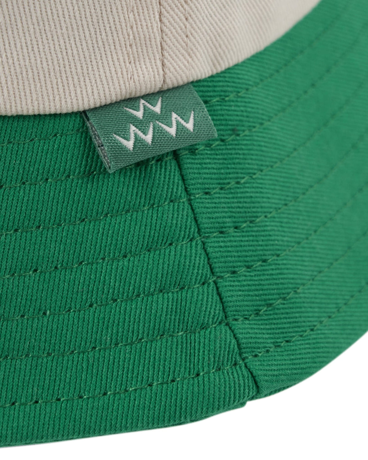 Detail of an off-white and green bucket hat with a small stitched tag showing three white zig-zags.