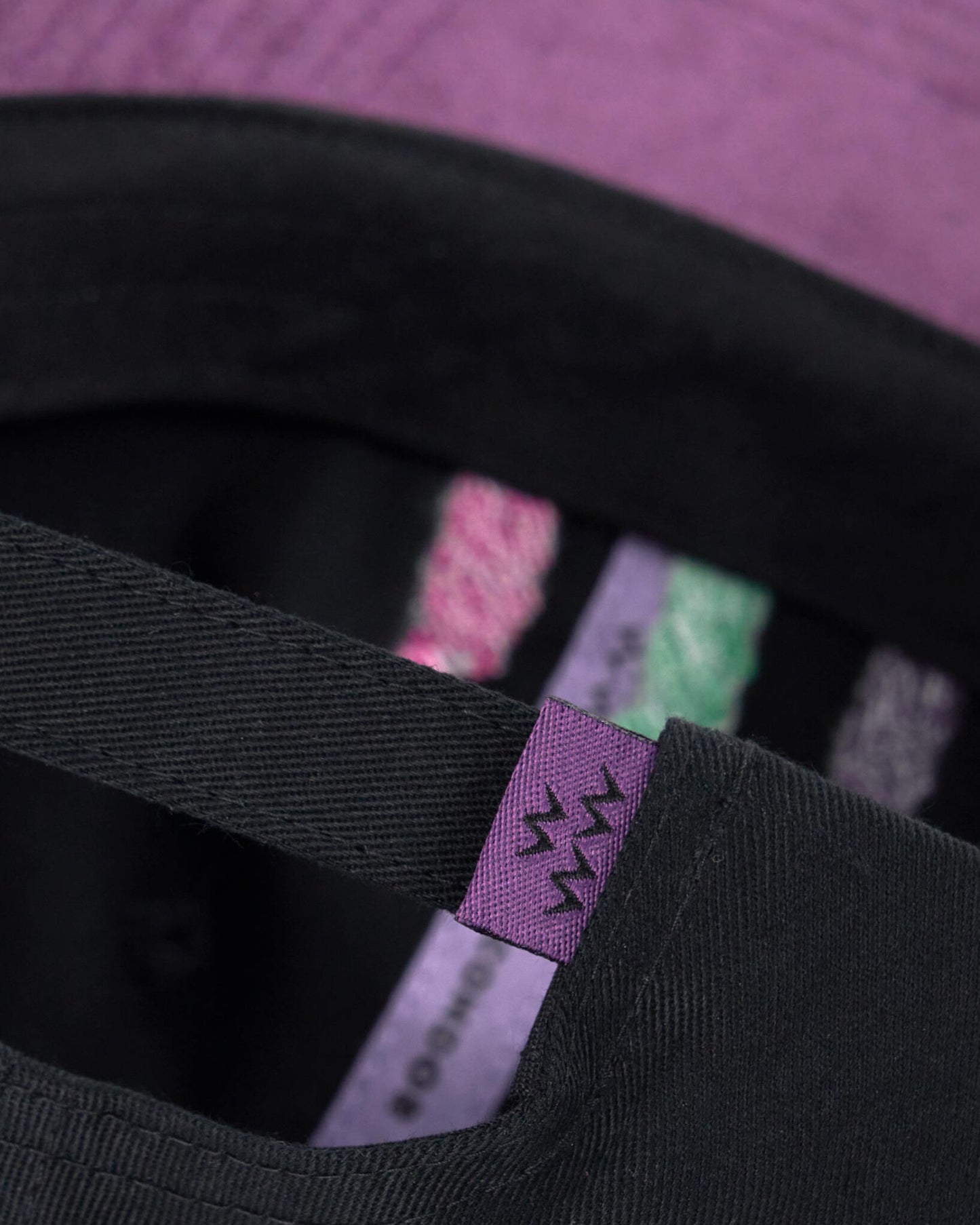 Detail of a black cap with a purple strap and a purple buckle, showing inner printed tape.