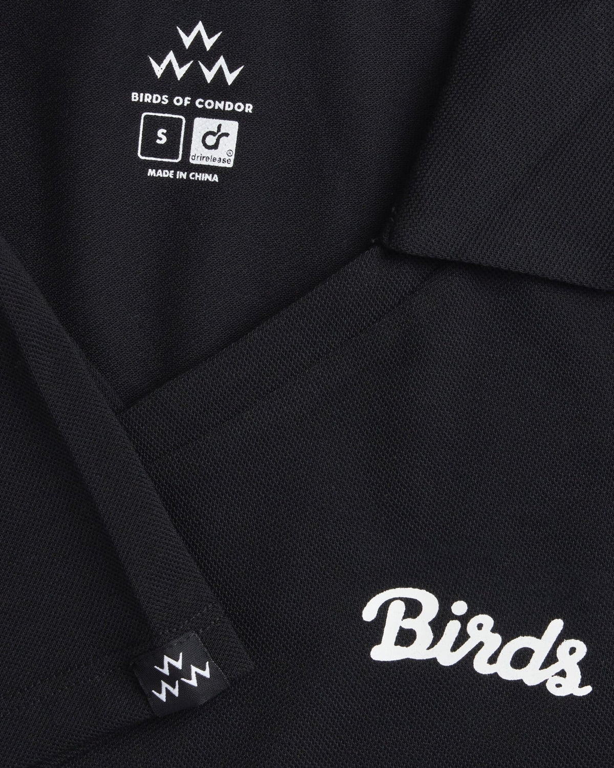 Detail of a black polo shirt featuring a white cursive logo and printed inner neck labels.
