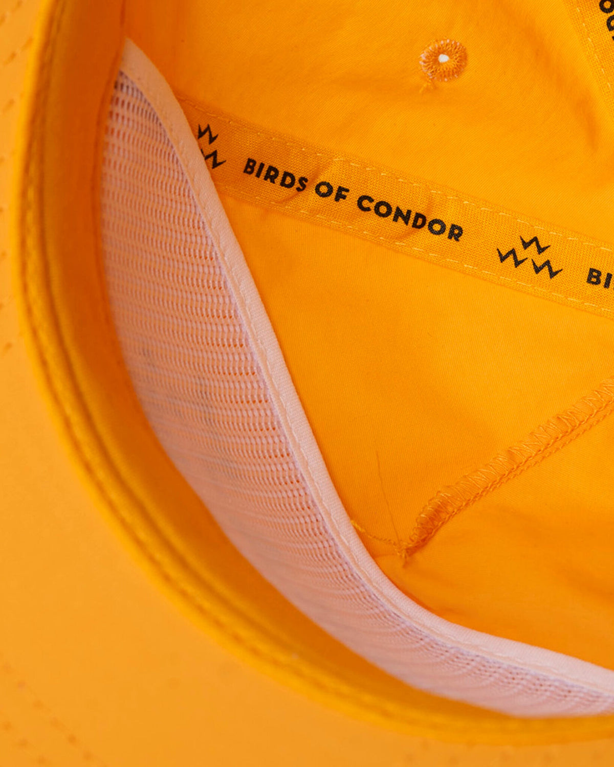 Detail of a yellow cap featuring interior white mesh paneling and branded seam taping.
