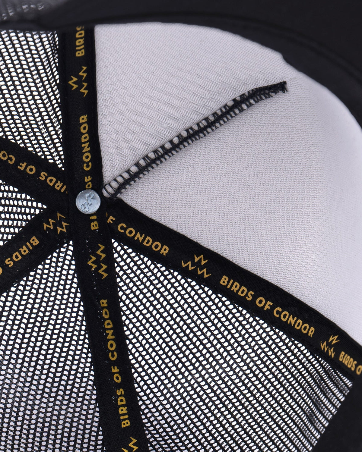 Detail of the interior crown of a black trucker hat showing branded black taping with gold text.