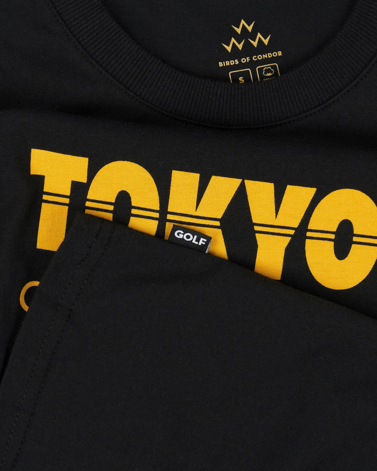 Detail of a black cotton t-shirt featuring yellow text and a small black tag labeled GOLF.