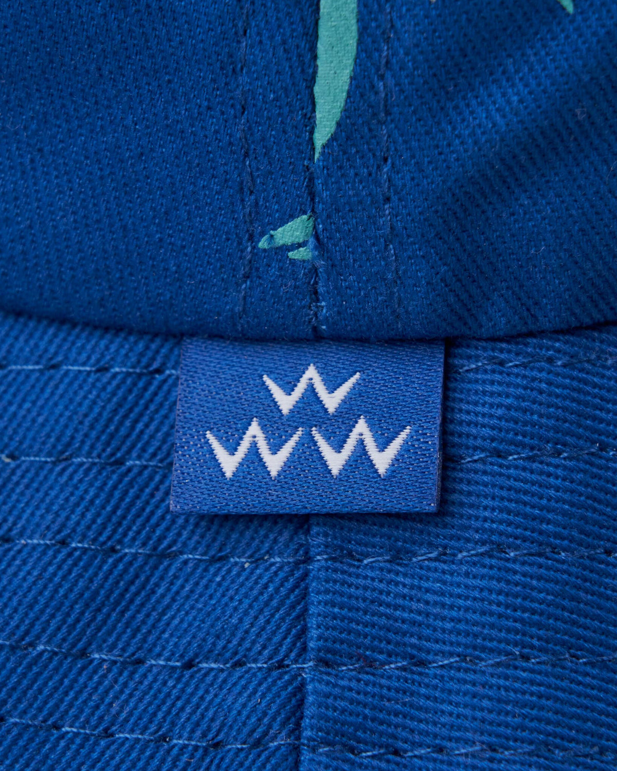 Detail of a blue bucket hat showing a small blue label with white W motifs.