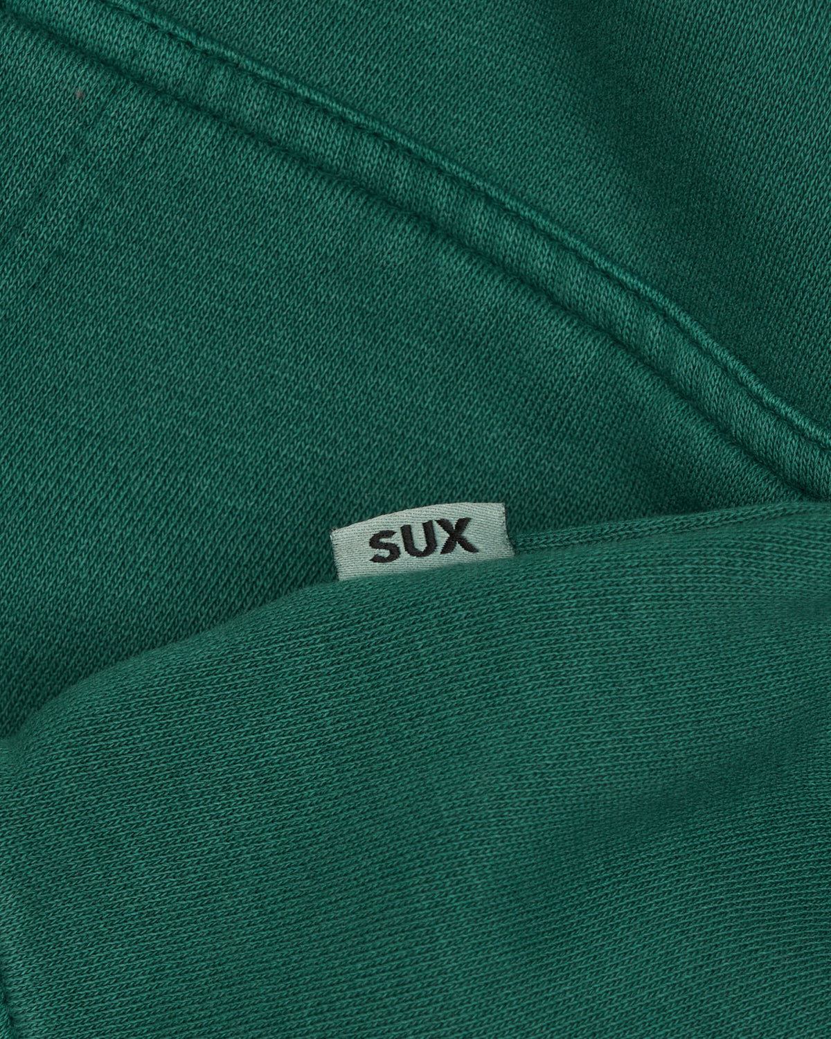 Detail of a green hoodie with a small white side tag displaying the text SUX.