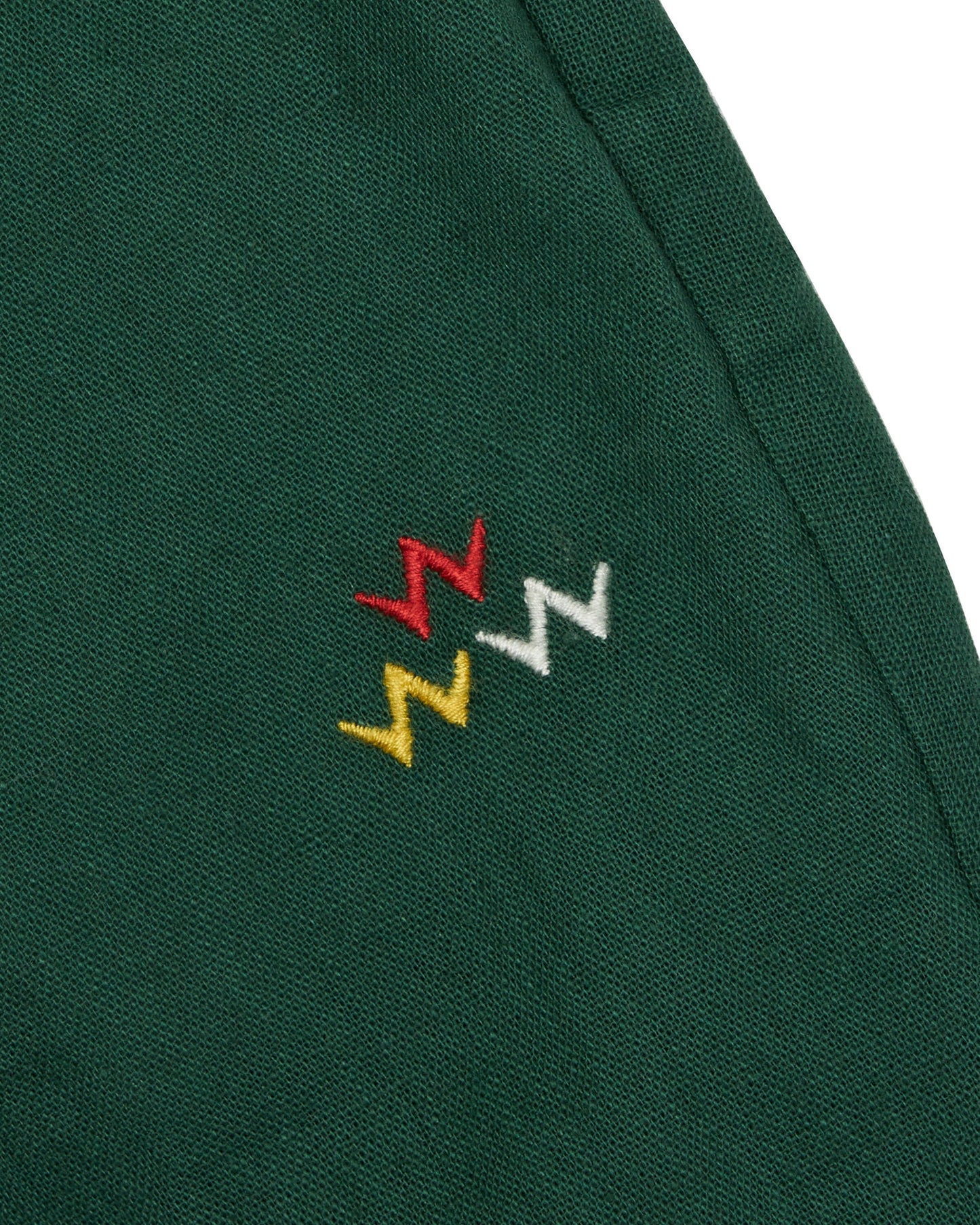 Detail of dark green linen blend pants featuring an embroidered tri-colour Triple Eagle logo.