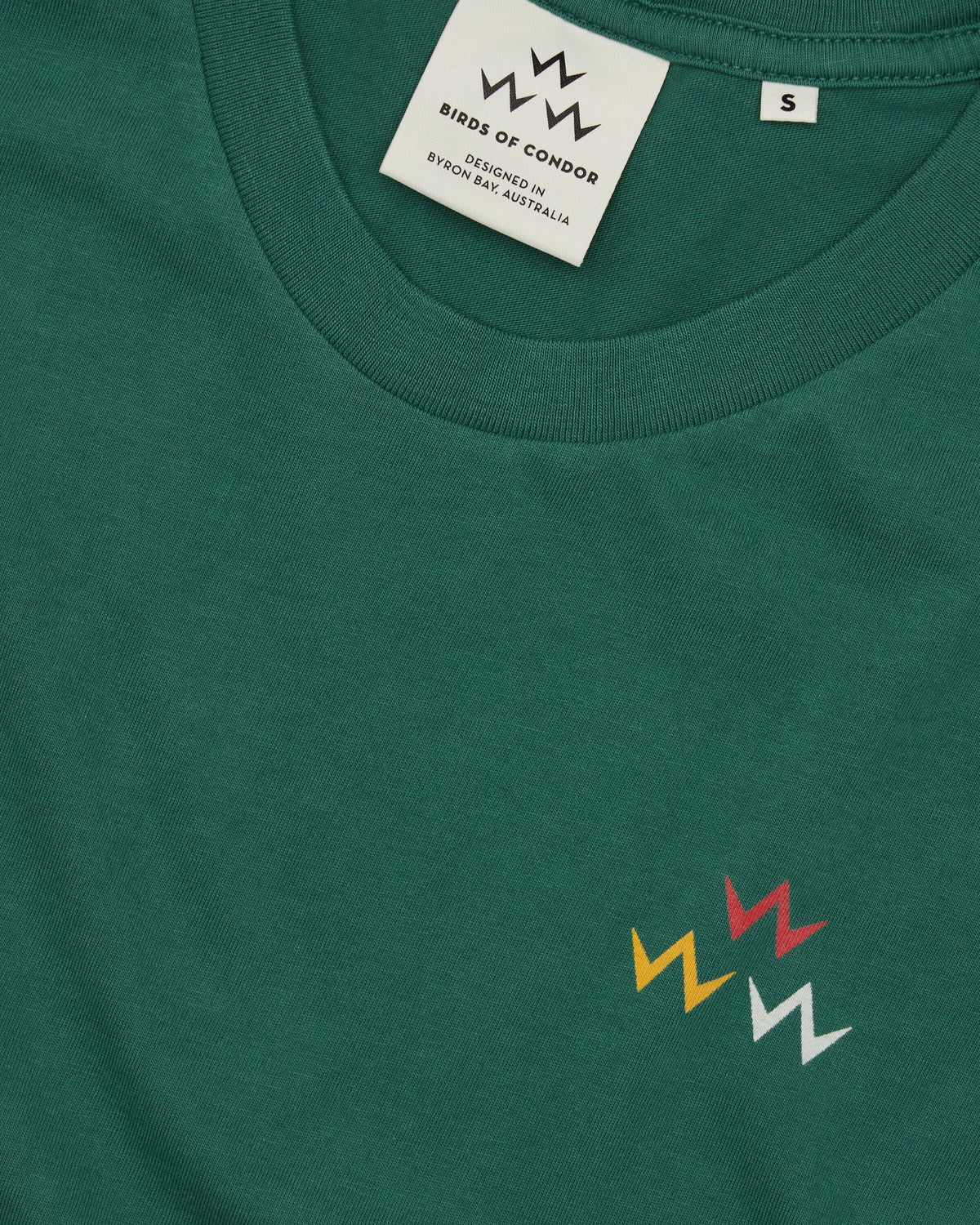 Detail of a green t-shirt with a triple eagle logo print and inner collar branding tags.