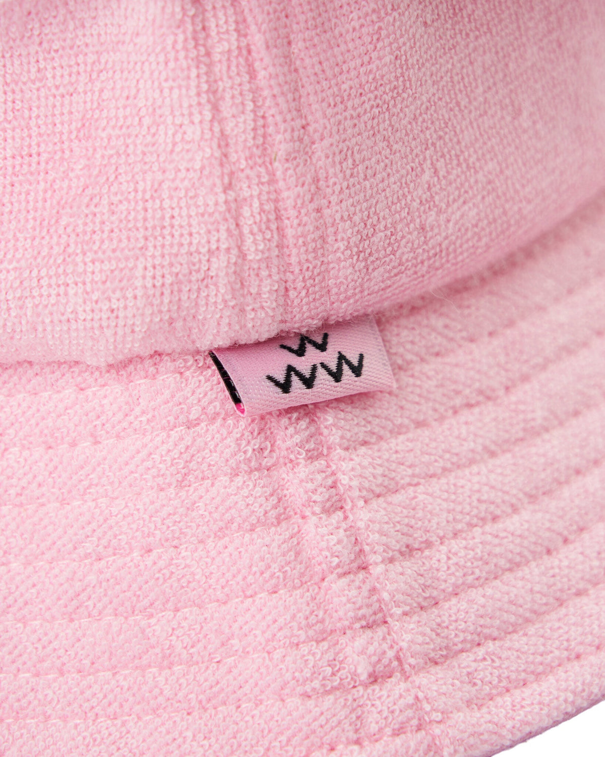 Detail of pink terry cloth bucket hat featuring a small sewn label with black wavy letter branding.