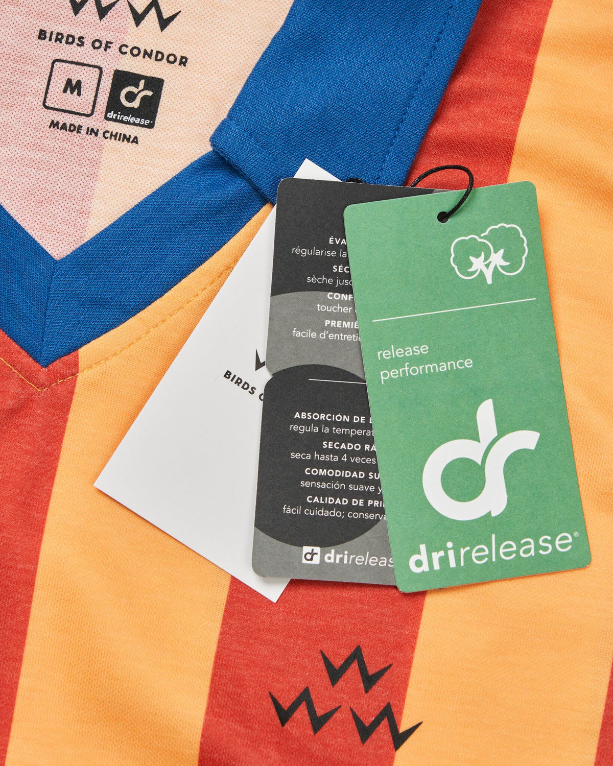 Detail of red and yellow striped polo shirt with blue V-neck collar, branded tags, and a black bird motif.