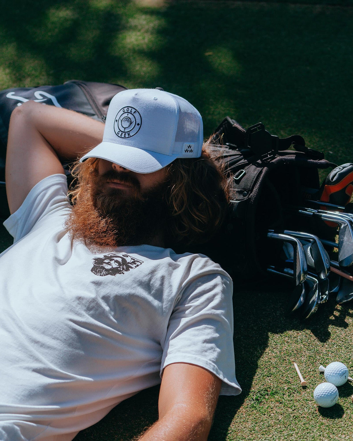 A man wearing a white snapback hat with a round Golf Geek logo on the front crown, outdoors.