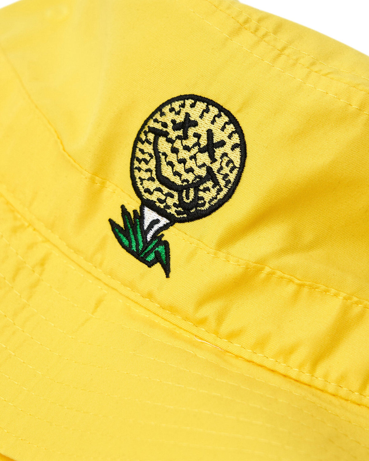 Detail of a yellow bucket hat with an embroidered golf ball tee smiley face design on the front.