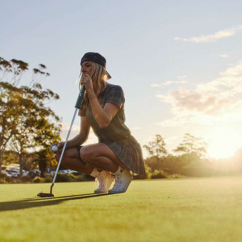 Woman on a golf course preparing to putt with sunset in the background