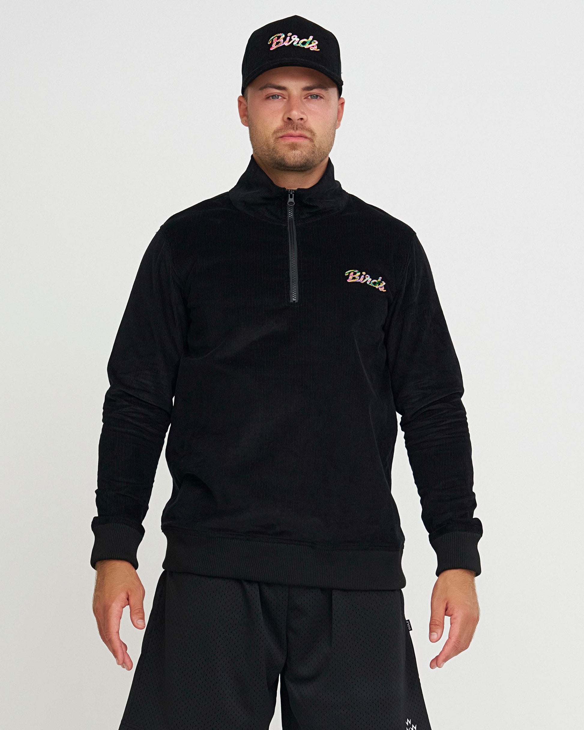 Man wearing a black outfit with colourful 'Birds' script embroidered on the chest