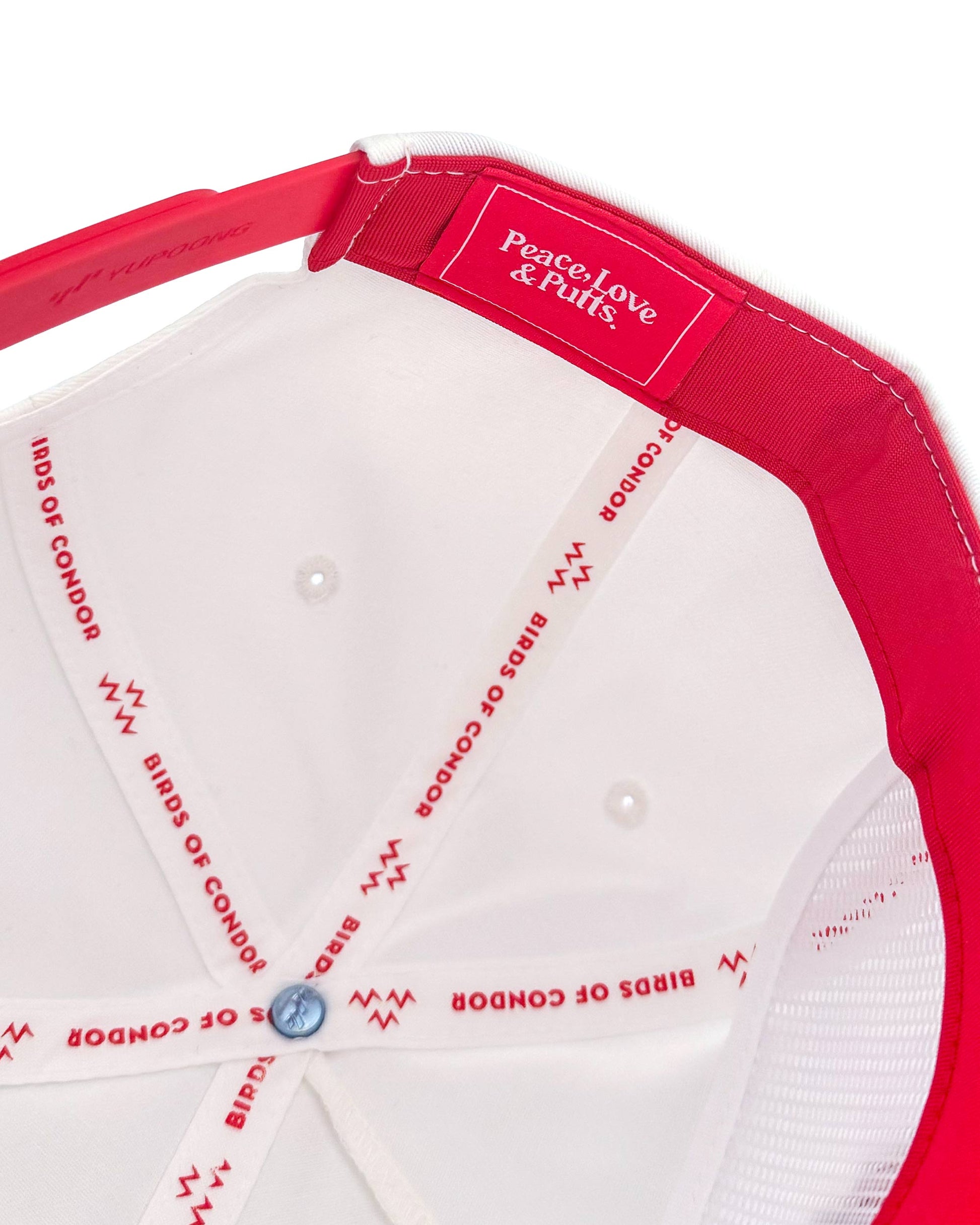 Close-up of a red and white cap with 'Peace Love & Putts' branding on a white background.