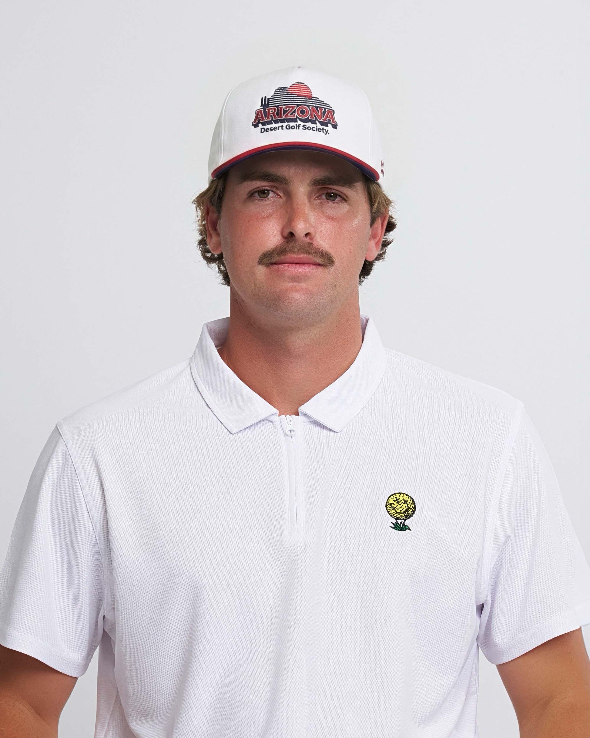 Man wearing a white polo shirt with a neverfind golf logo and a cap with 'Arizona Desert Golf Society' text on a plain background