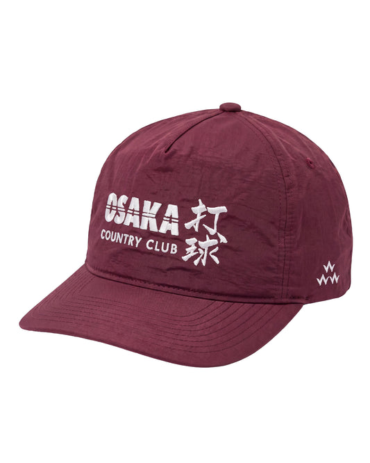 A maroon baseball cap featuring white embroidered text on the front that reads 'OSAKA COUNTRY CLUB' alongside Japanese characters, and a small white logo on the side, set against a plain white background.