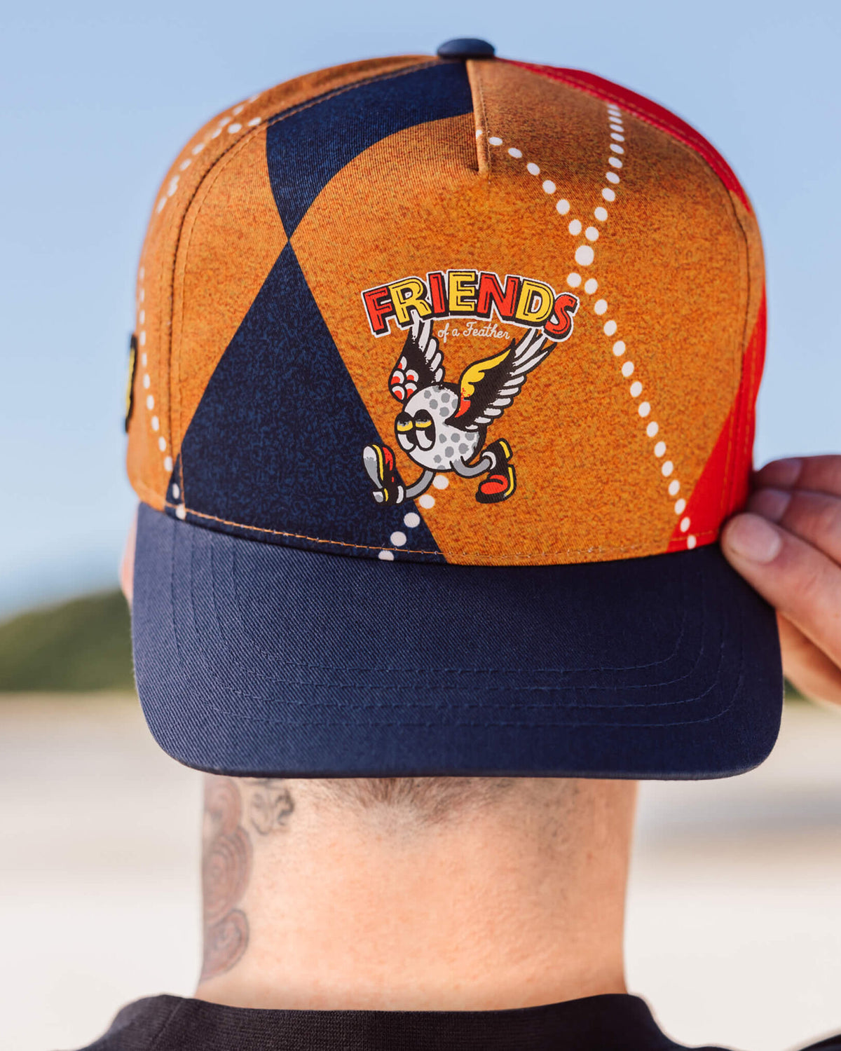 Front of an argyle snapback hat featuring a cartoon bird graphic and navy blue flat brim.