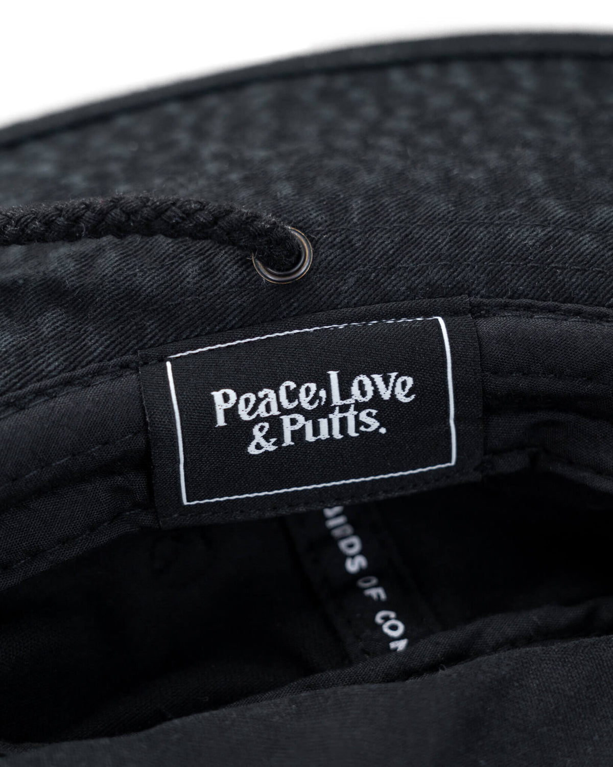 Detail of a black boonie hat featuring an inner woven label reading Peace, Love & Putts in white text.