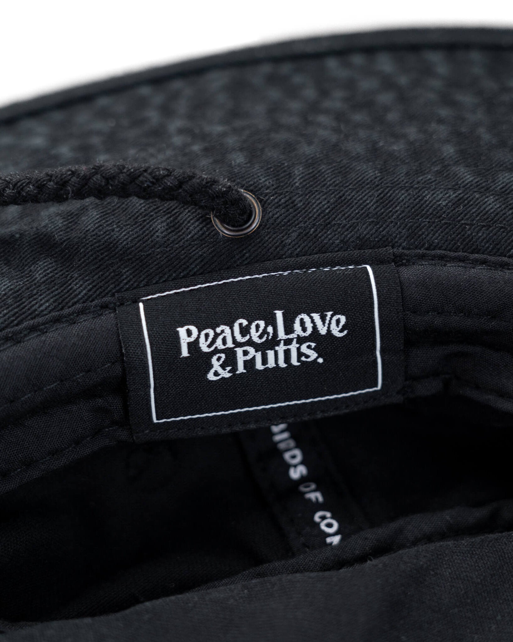 Detail of a black boonie hat featuring an inner woven label reading Peace, Love & Putts in white text.