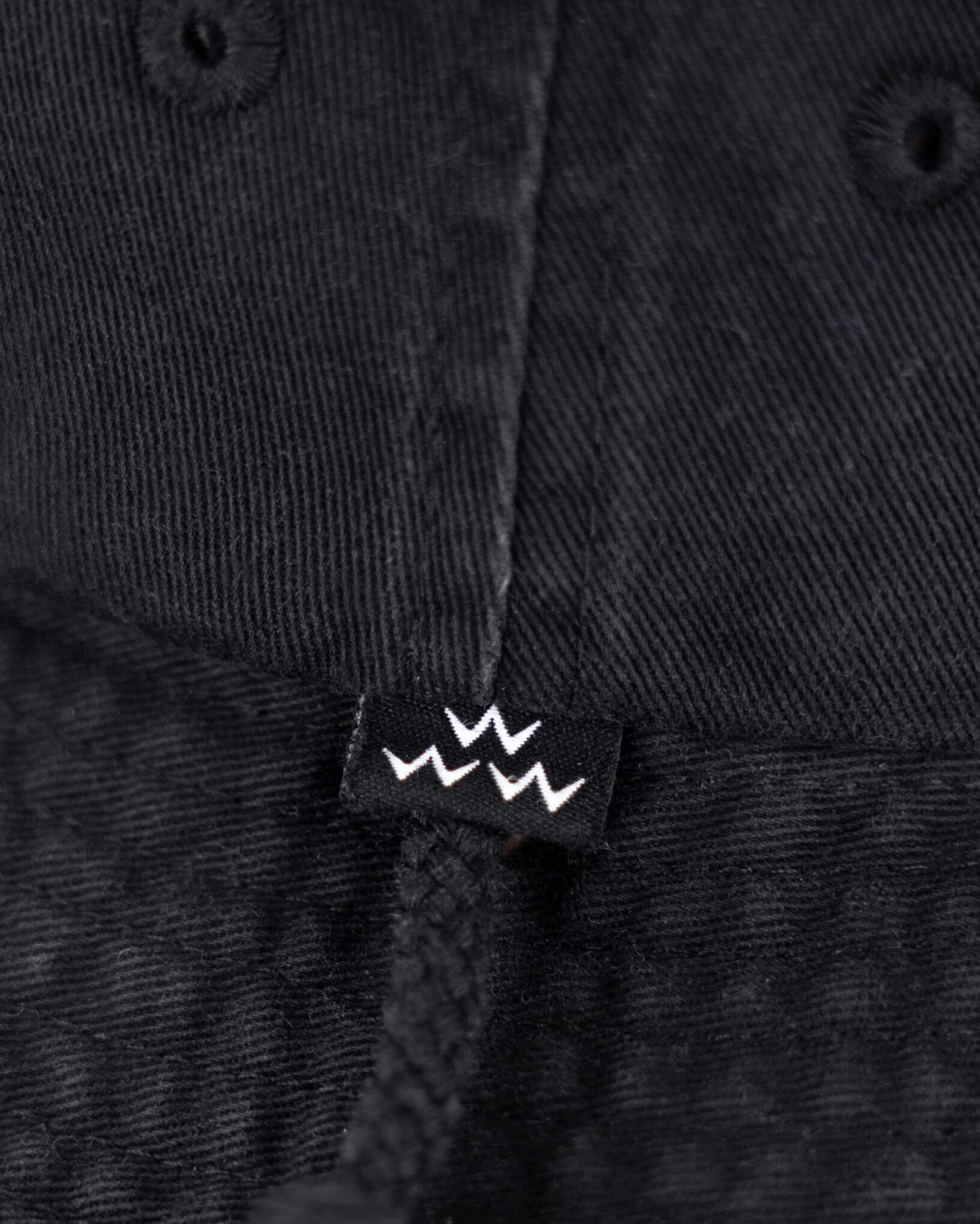 Detail of a black boonie hat featuring a small black label with three white crown outlines and a drawstring.
