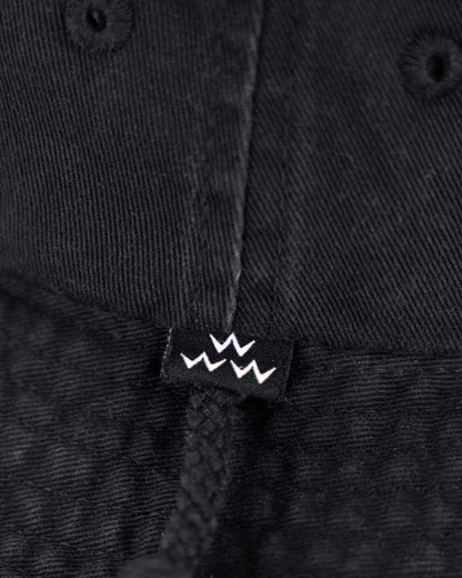 Detail of a black boonie hat featuring a small black label with three white crown outlines and a drawstring.