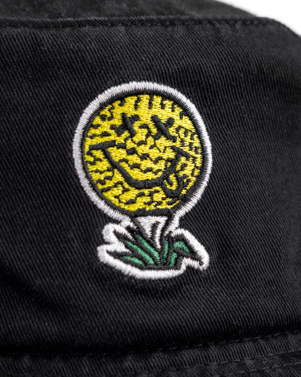 Detail of a black boonie hat featuring a yellow golf ball smiley face logo on a tee with green grass.