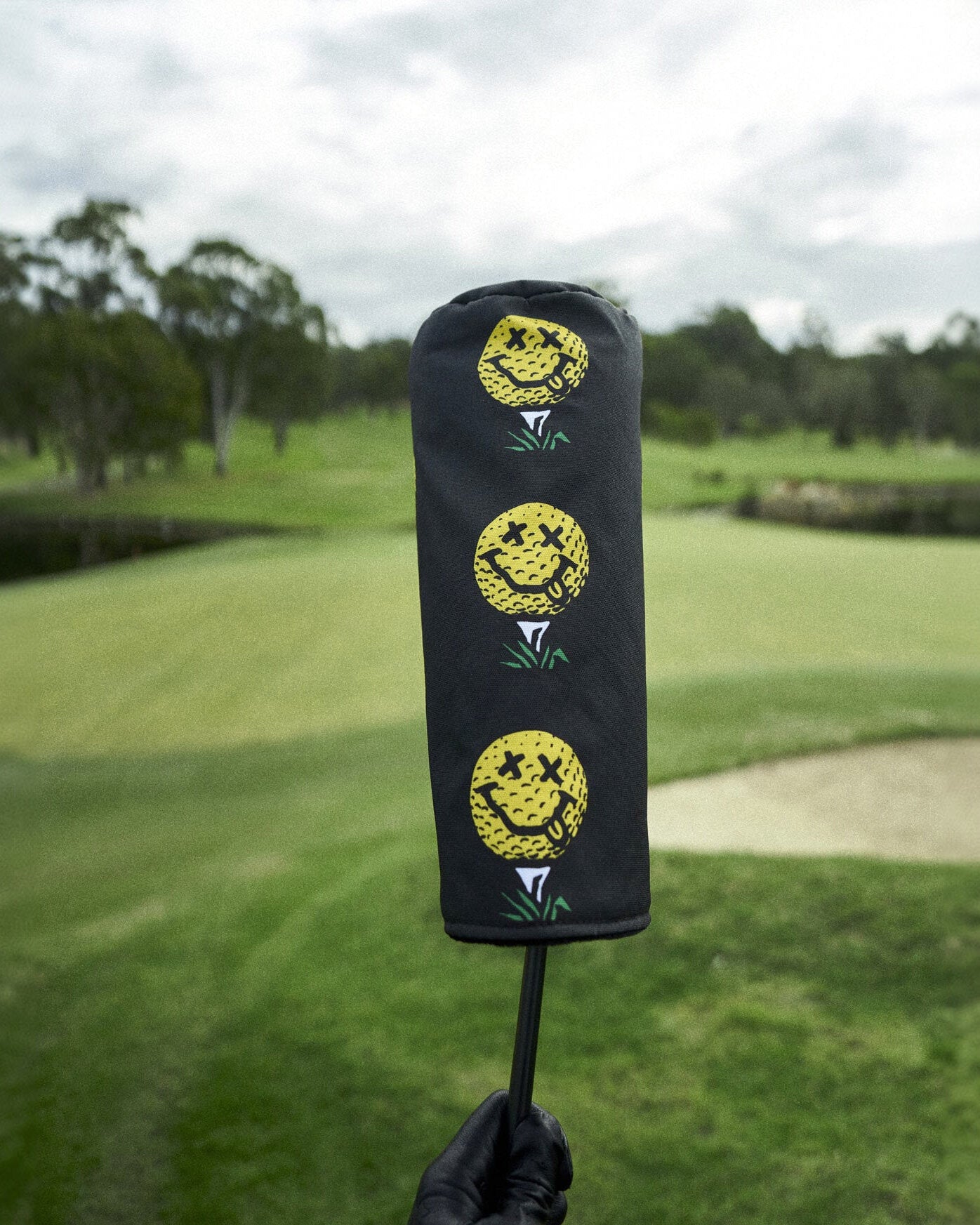 Black golf headcover featuring a vertical stack of three yellow smiley face golf ball graphics.