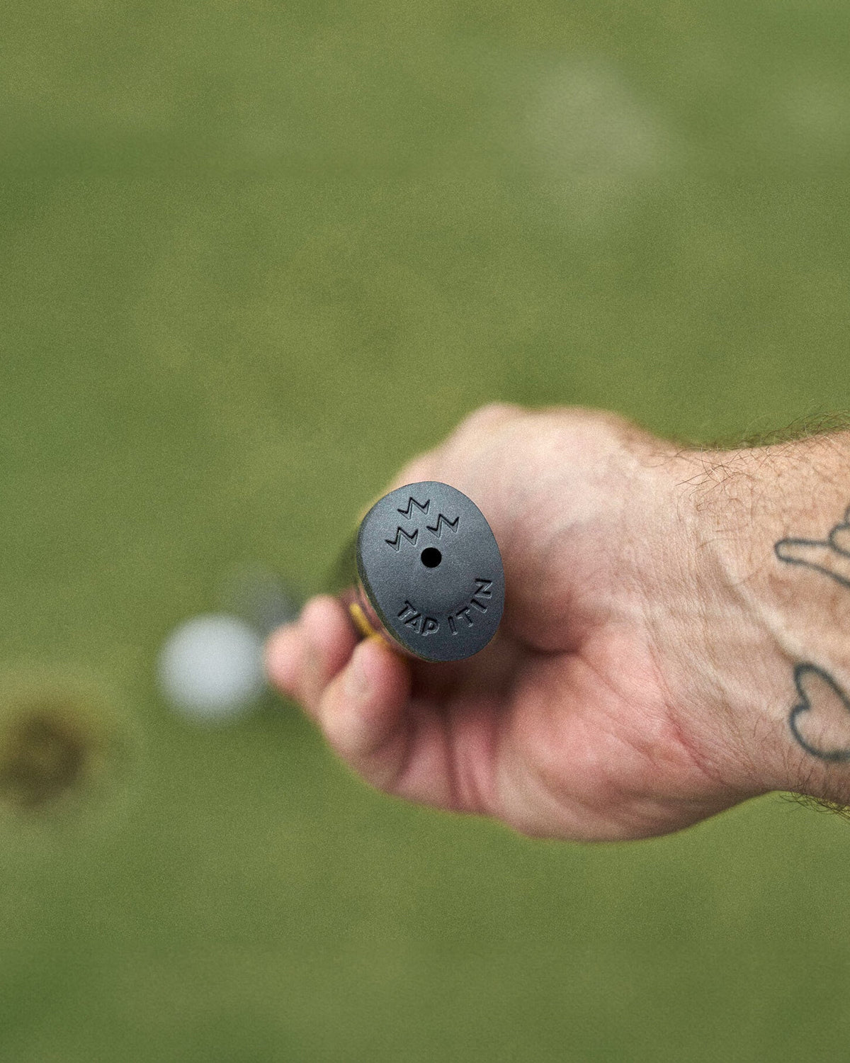 A hand holding a black putter grip with a triple eagle logo and the words Tap It In on the end.