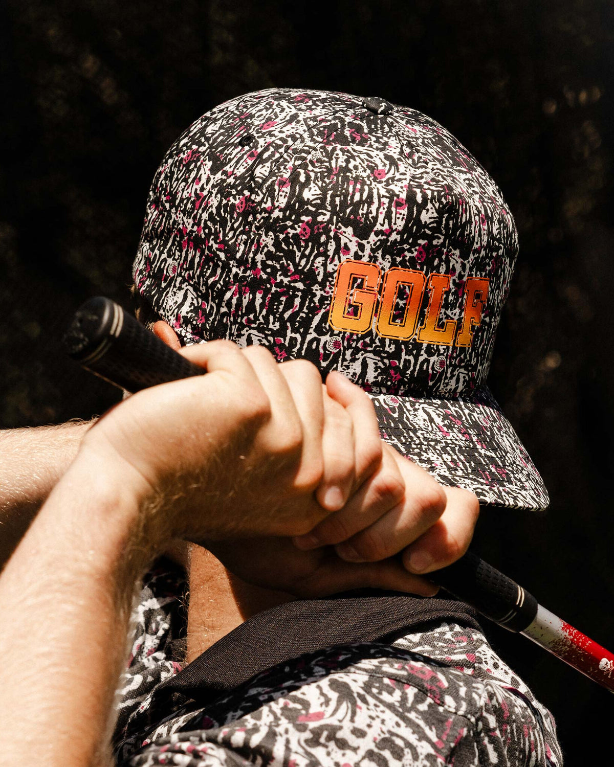A person wearing a black motley cap featuring a yellow fade GOLF print on the front and a curved brim.