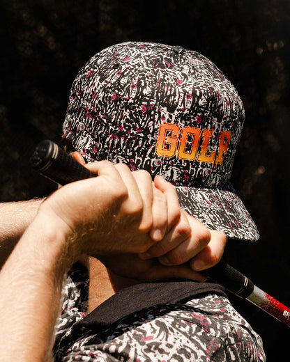 A person wearing a black motley cap featuring a yellow fade GOLF print on the front and a curved brim.