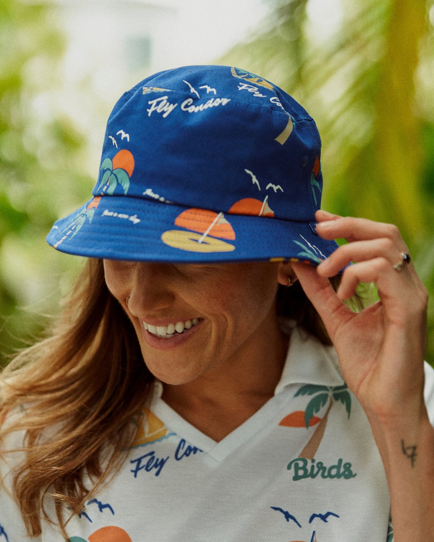 A woman wearing a blue cotton bucket hat with a repeat tropical print of sailboats and palms.