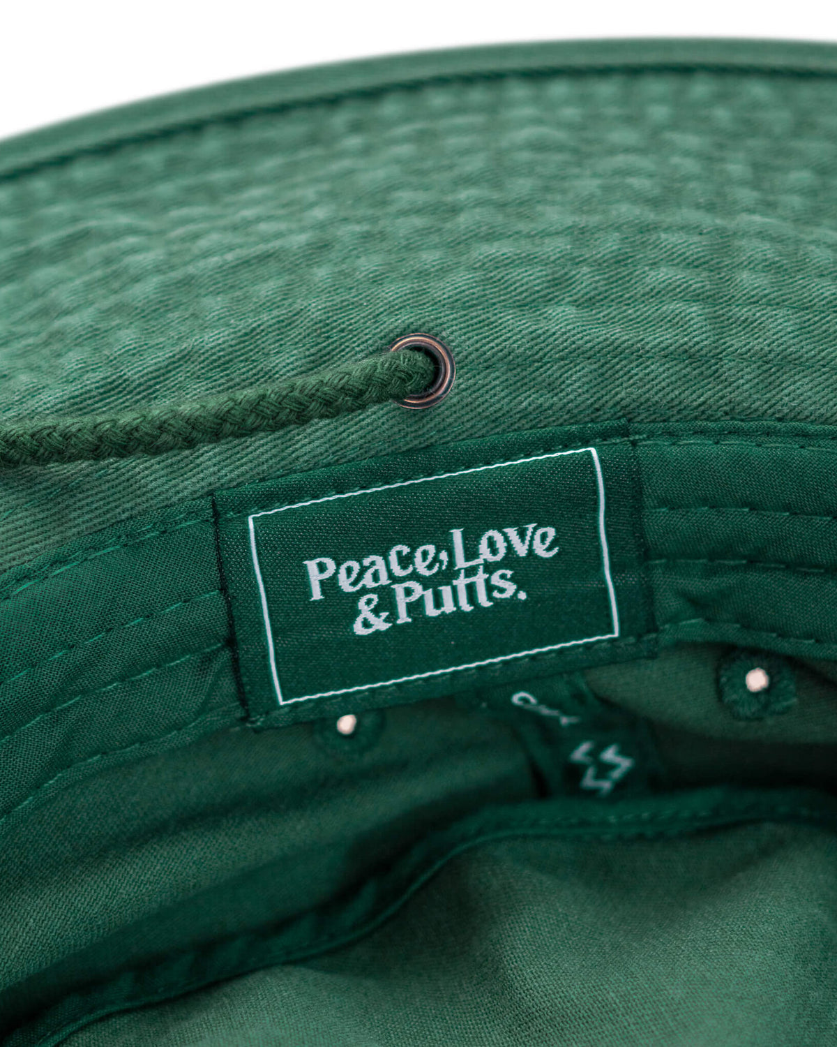 Detail of a green boonie hat featuring an interior woven label with white Peace, Love & Putts. text.