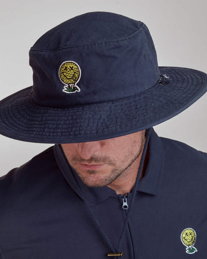 A man wearing a navy boonie hat with a yellow smiley golf ball graphic and a drawstring chin strap.