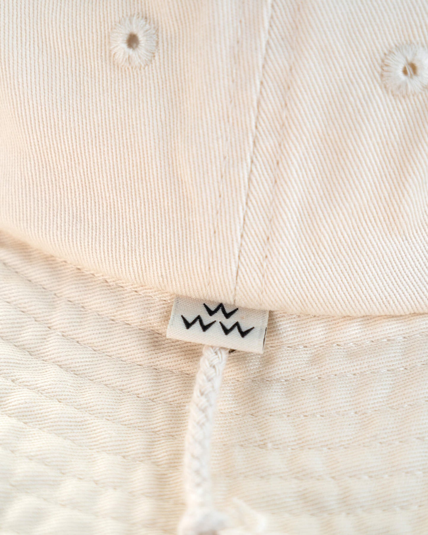 Detail of an off-white boonie featuring a small white tag with three black W symbols above the chin strap.