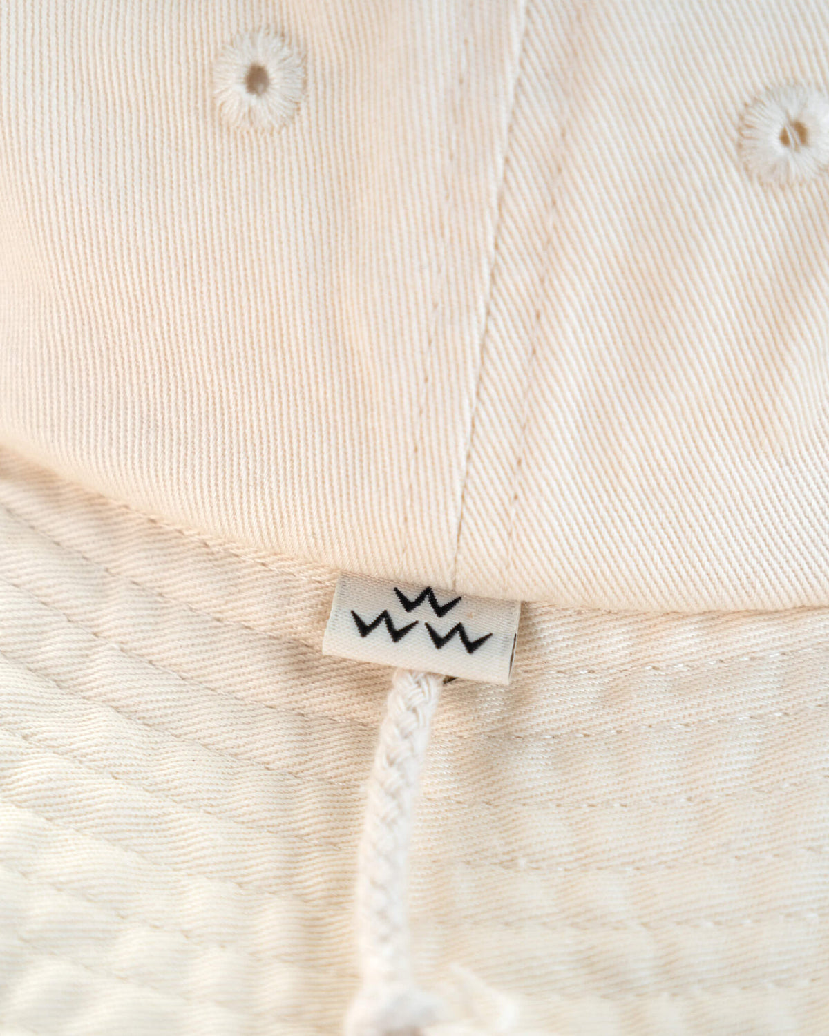 Detail of an off-white boonie featuring a small white tag with three black W symbols above the chin strap.