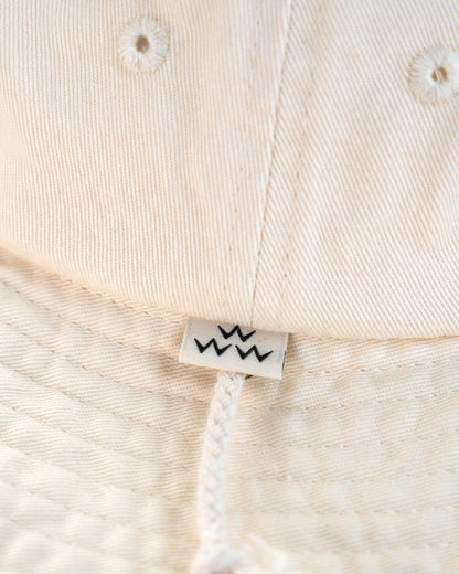 Detail of an off-white boonie featuring a small white tag with three black W symbols above the chin strap.