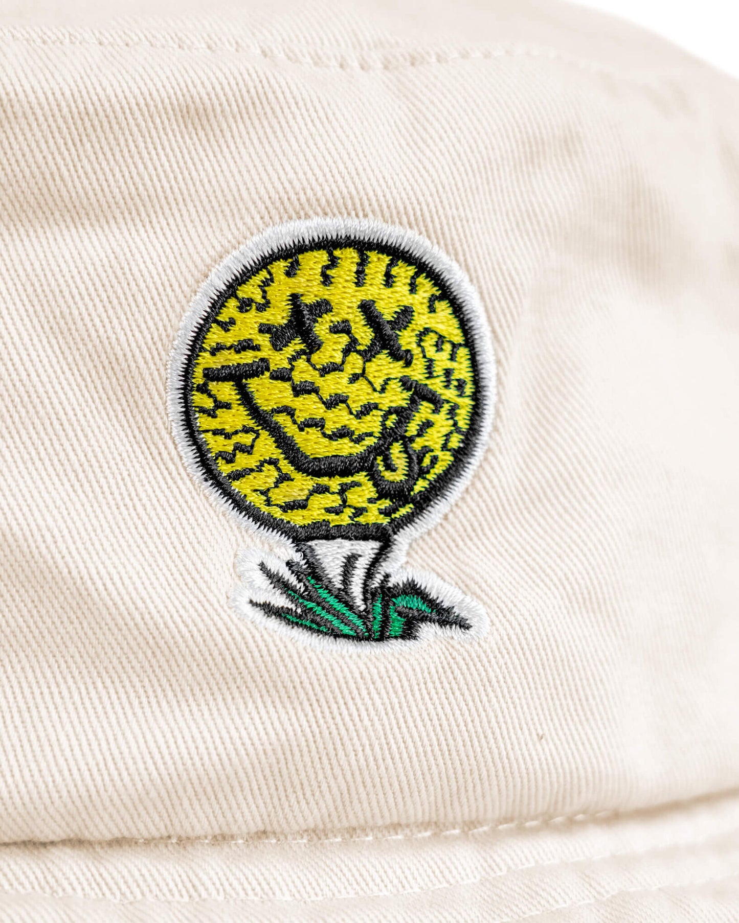 Detail of an off-white cotton boonie featuring a smiley face golf ball design on a tee.